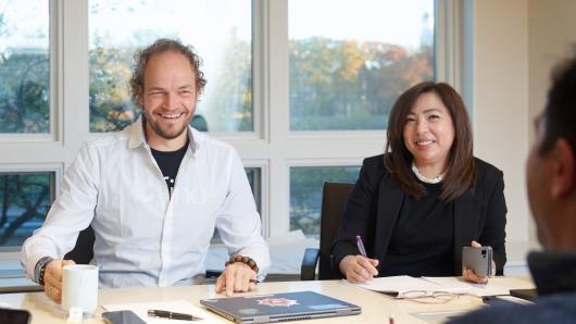 Male and female executive sit engaged at a table listening to their peer speak.