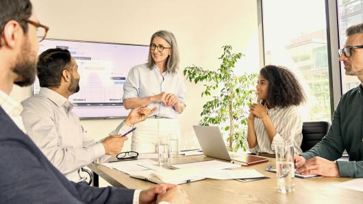 A group of smiling business people gather around a conference room table.