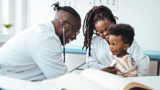 African American doctor using stethoscope on your boy sitting in mother's lap