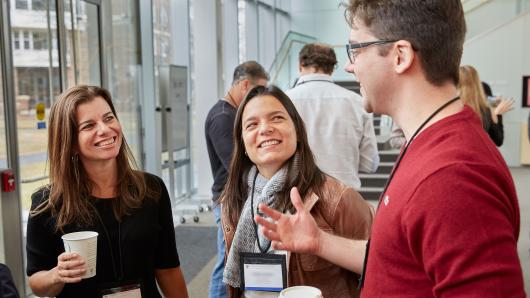 Two female executives and one male executive conversing in the Tata Hall atrium