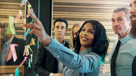 a diverse group of young executives interacting with a post-it board